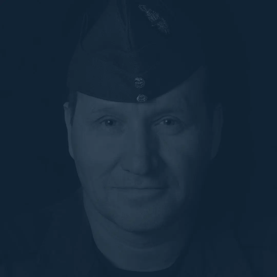 Sur un fond noir, on voit le visage du capitaine Gérard Caron portant le calot bleu roi de l’Aviation royale canadienne. Il regarde la caméra avec un léger sourire.