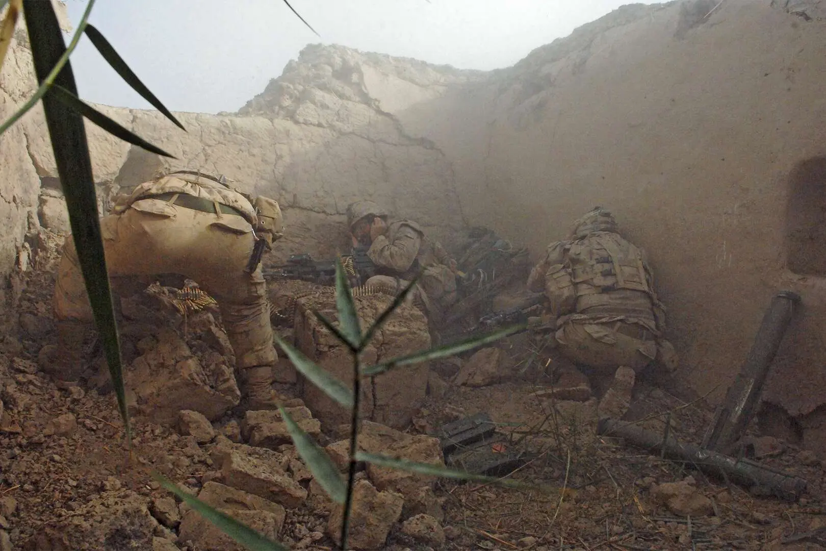 Trois militaires canadiens se mettent à l’abri des combats dans un bâtiment détruit et abandonné, sans toit et jonché de divers débris au sol. Des armes et des balles traînent autour d’eux.