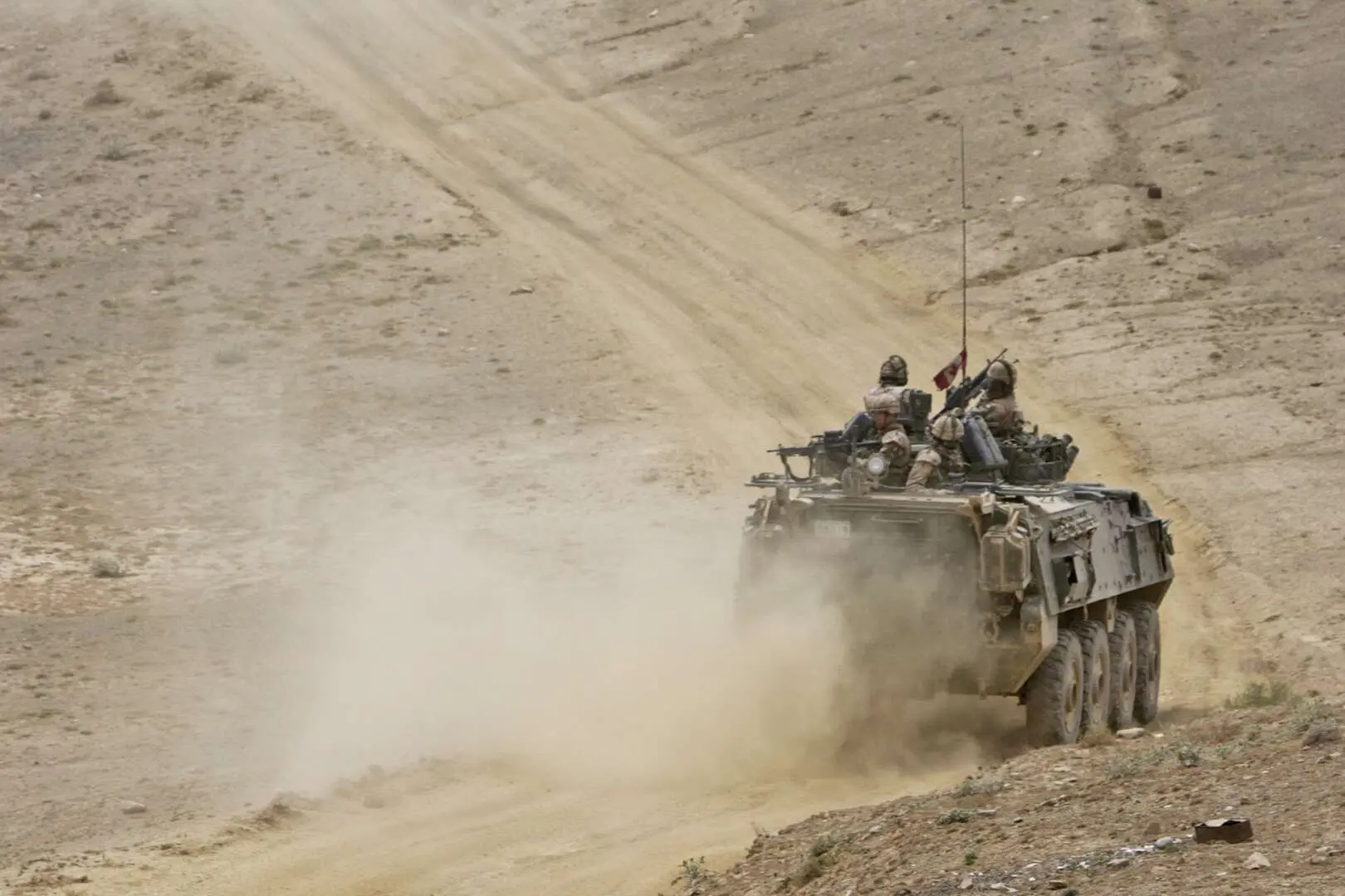 Deux véhicules blindés du Royal 22ième Régiment montent une pente sinueuse et poussiéreuse dans une montagne. Des soldats sont visibles au sommet des deux véhicules de combat.