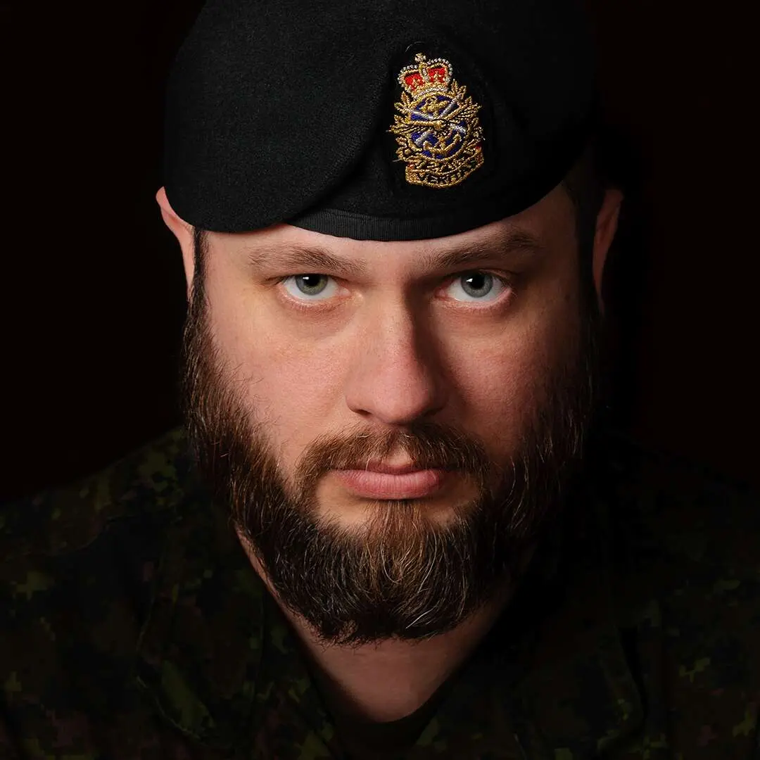 Sur un fond noir, on voit le sergent Gary Calvé. Son visage est ovale et ses yeux verts. Il porte le béret vert foncé de l’Armée canadienne. Il regarde la caméra d’un air sévère.