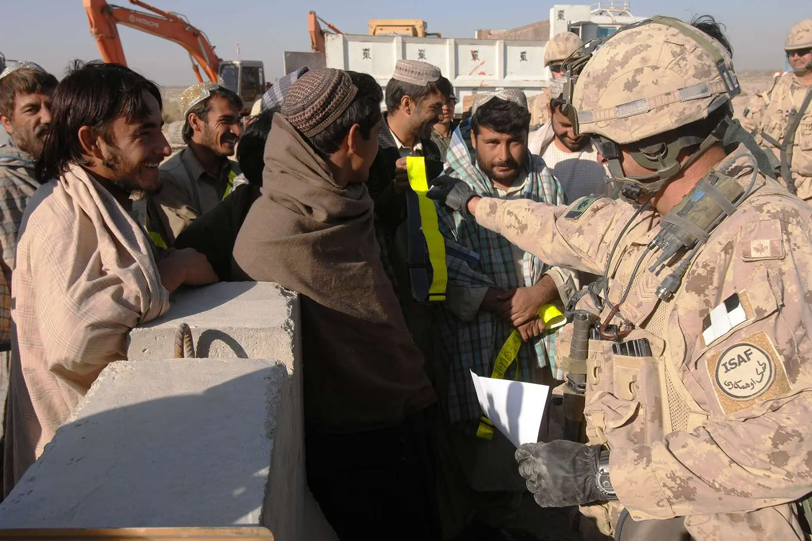 Sur un chantier, un militaire canadien distribue des ceintures réfléchissantes jaunes à une dizaine d’ouvriers civils afghans.