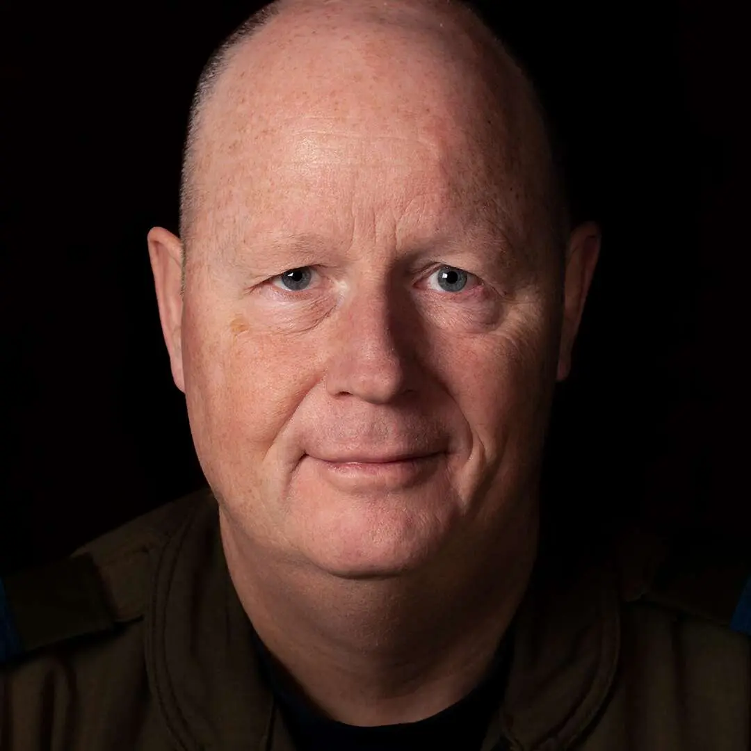 Sur un fond noir, on voit le major Alain Tanguay. Chauve avec un visage ovale, il sourit à la caméra.