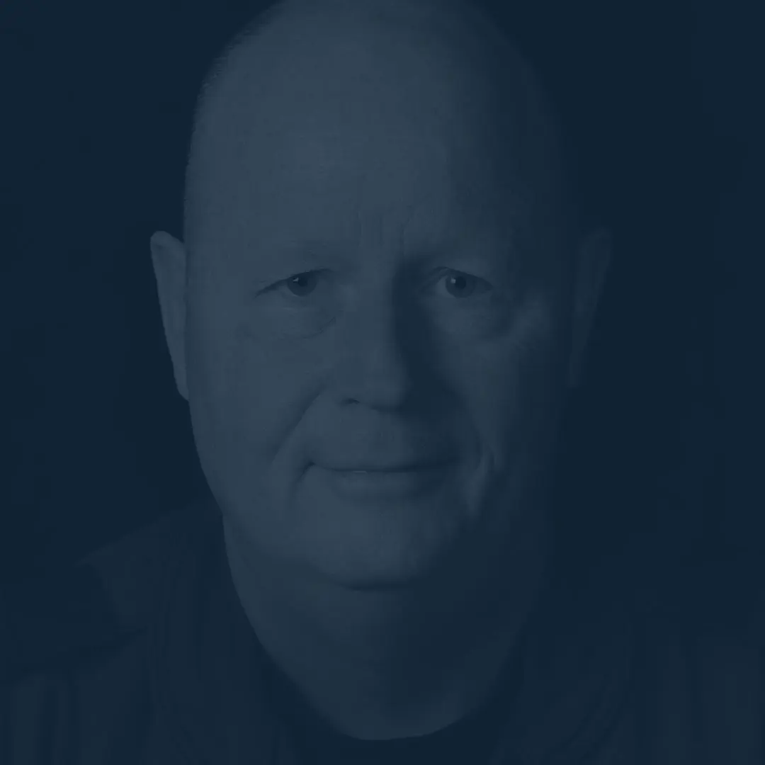 Sur un fond noir, on voit le major Alain Tanguay. Chauve avec un visage ovale, il sourit à la caméra.