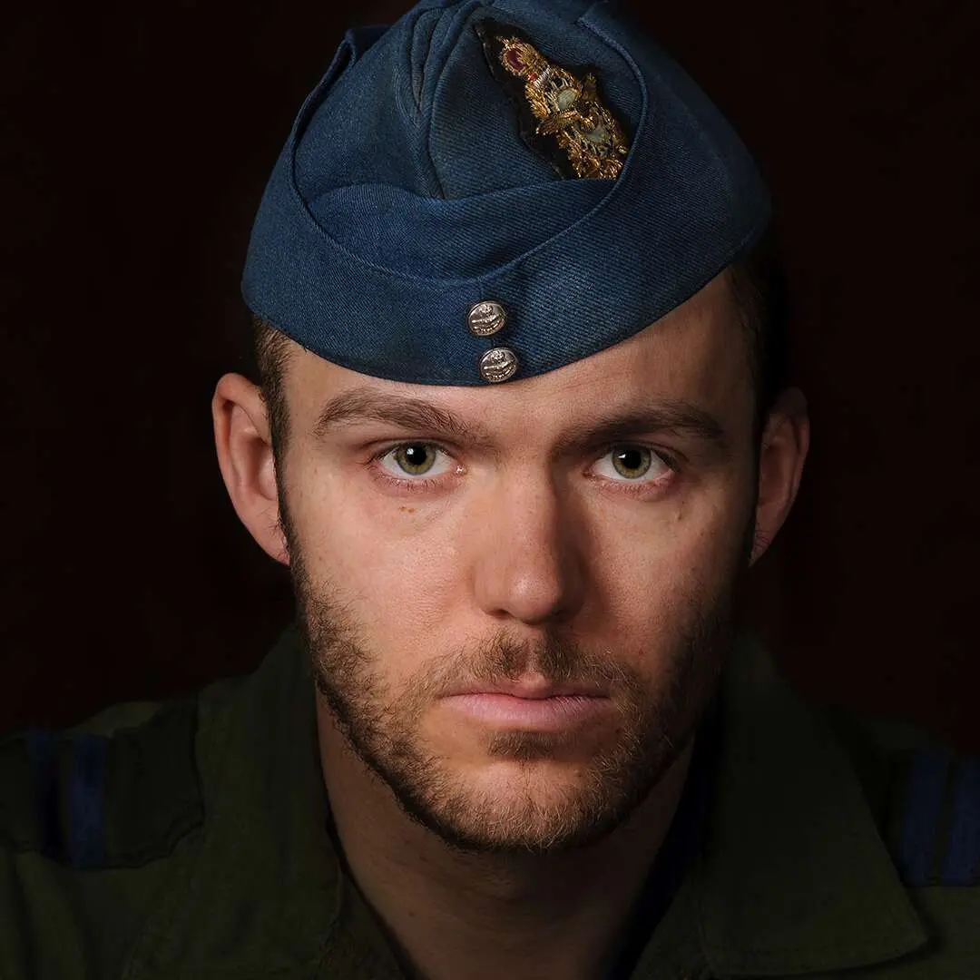 Sur un fond noir, portant le calot bleu roi de l’Aviation royale canadienne et affichant une barbe claire, le capitaine DHG fait face à la caméra avec un regard impénétrable. 