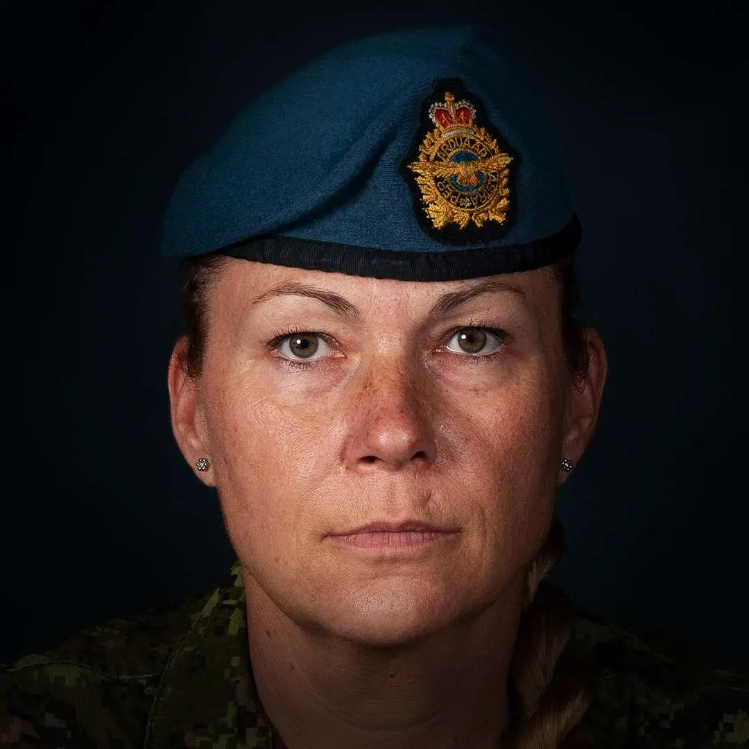 Sur un fond noir, la caporale Cindy Bergeron affiche un visage ovale et basané. Ses cheveux blond-roux sont attachés derrière la tête. Elle porte son béret bleu de l’Aviation royale canadienne. 
