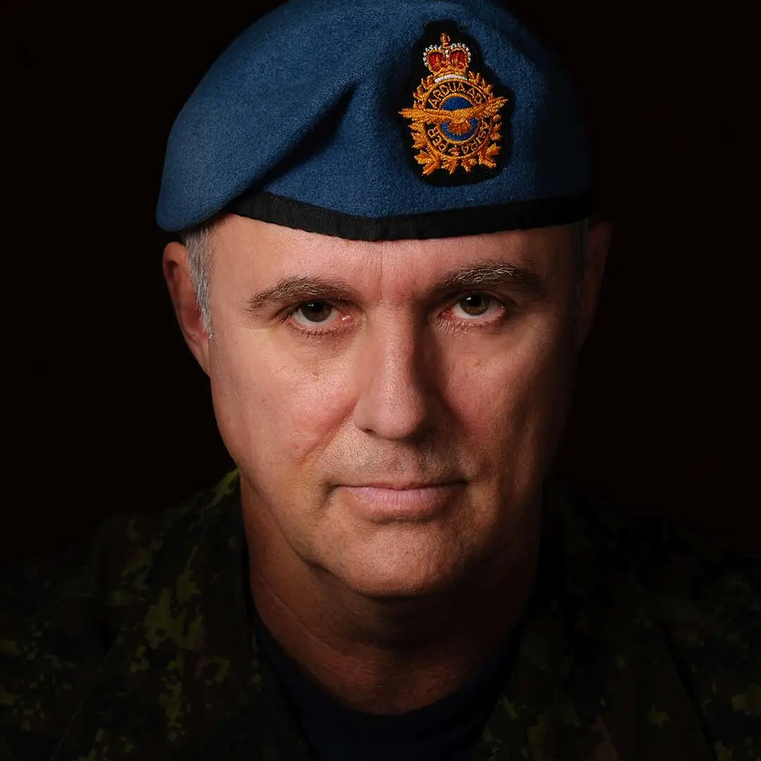 Sur un fond noir, le caporal Bernard Lachapelle regarde la caméra sérieusement. Il possède un visage triangulaire et porte un béret bleu de l’Aviation royale canadienne dissimulant ses tempes grisonnantes.