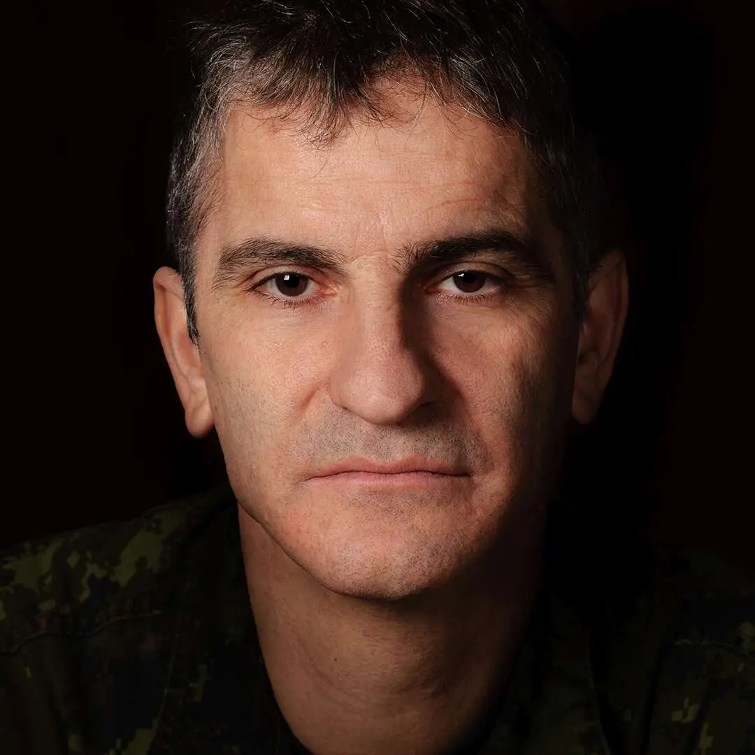 Sur un fond noir, l’adjudant Éric Henry, cheveux foncés, légèrement grisonnants, demeure impassible devant la caméra. 