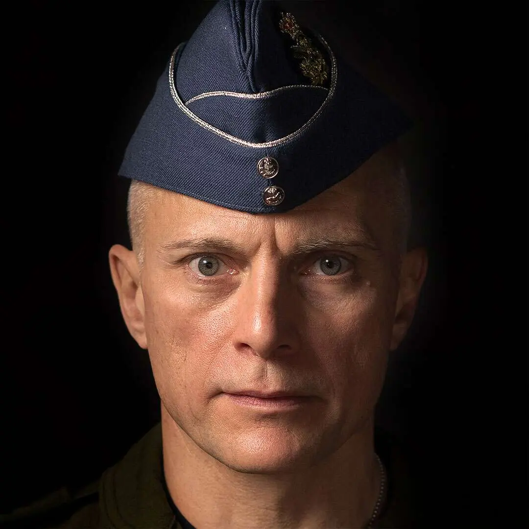 Sur un fond noir, le major-général Sylvain Ménard regarde froidement la caméra avec des yeux perçants. Il porte le calot bleu de l’Aviation royale canadienne.