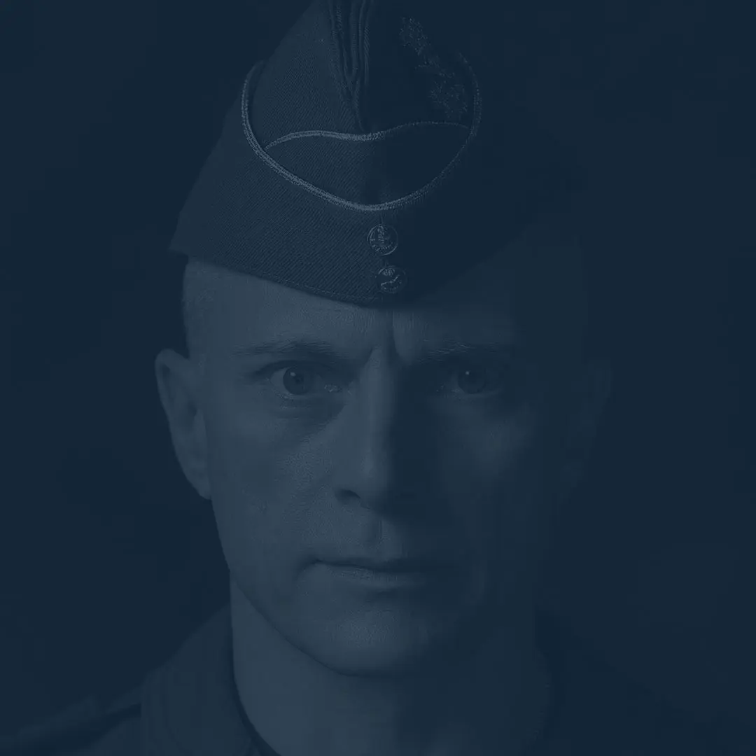 Sur un fond noir, le major-général Sylvain Ménard regarde froidement la caméra avec des yeux perçants. Il porte le calot bleu de l’Aviation royale canadienne.