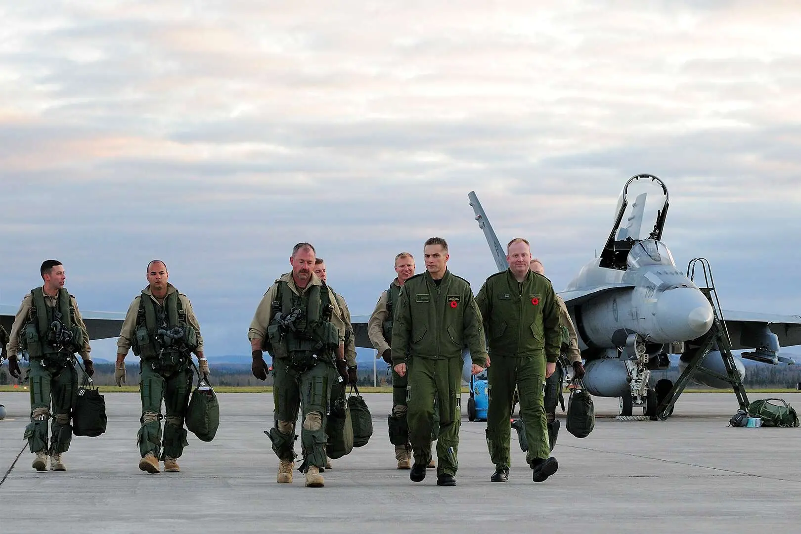 Sept pilotes canadiens marchent sur une piste d’avion. Un chasseur CF-18 Hornet est visible en arrière-plan.