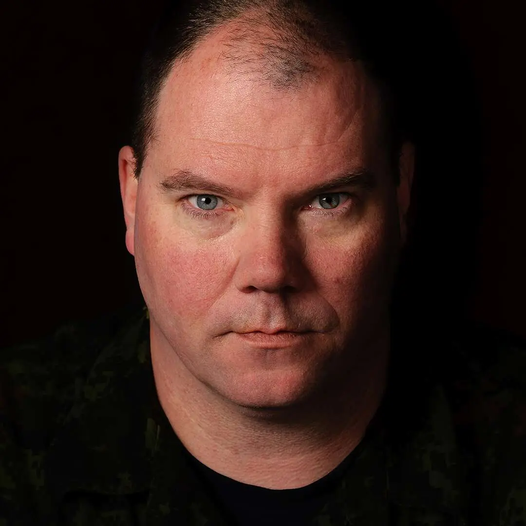 Sur un fond noir, le caporal Mark Vigneault, un homme au visage rond et aux yeux bleus, prend un air sérieux devant la caméra.