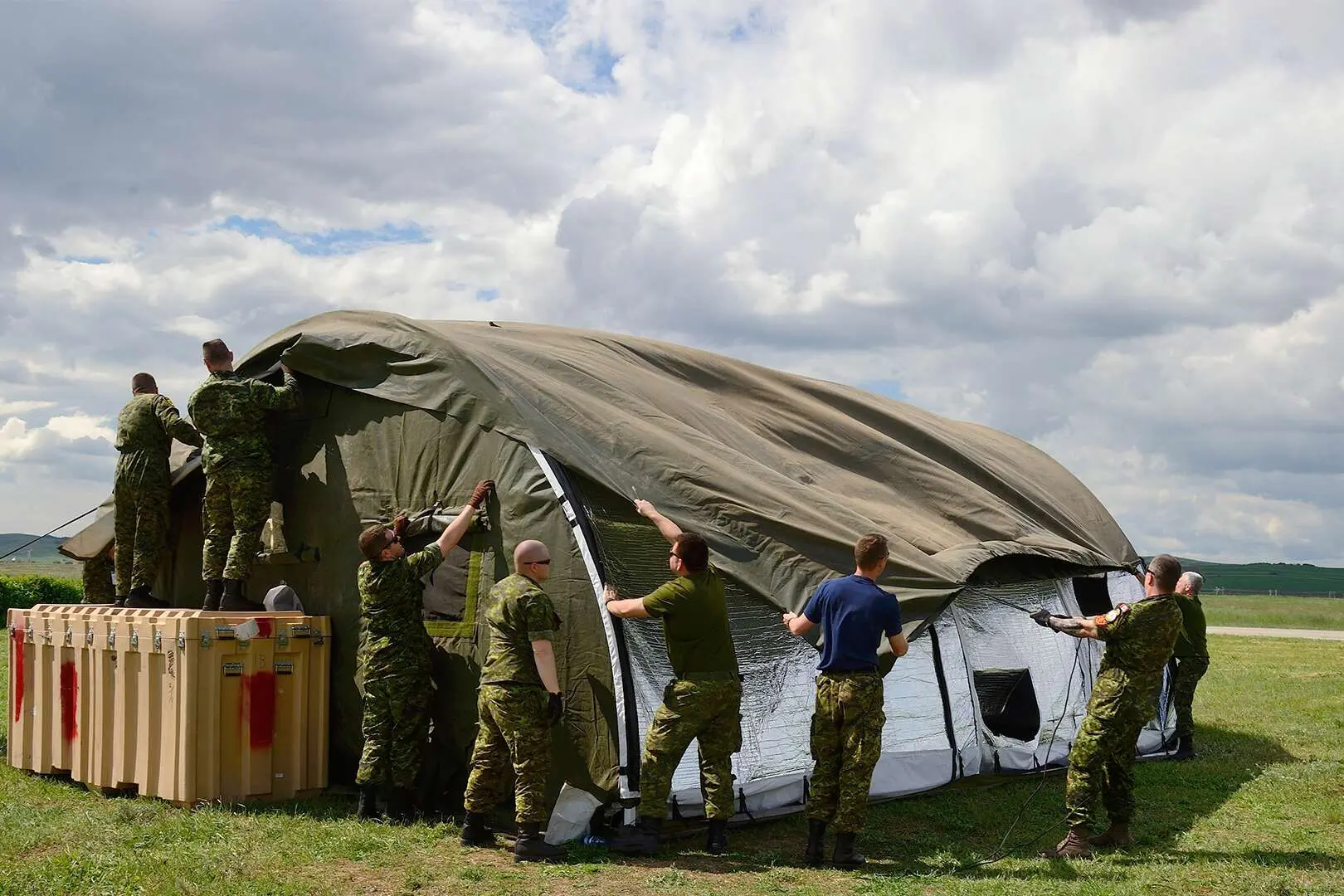 Neuf militaires canadiens s’activent à monter une tente temporaire sur un terrain gazonné.